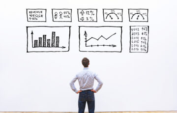 Business growth statistics illustrations on a wall with a man looking up at them, hands on hips